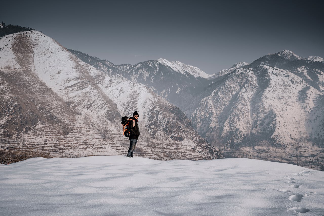 A backpacker stands amidst snow-covered mountains in Kashmir, enjoying a serene winter landscape.